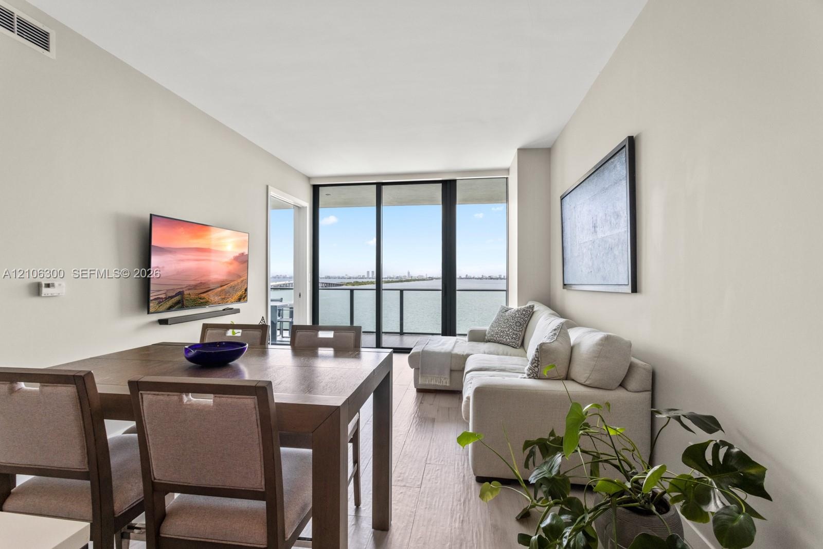 Living area with wood-finish flooring, floor-to-ceiling glass sliding doors, and a covered balcony overlooking the water