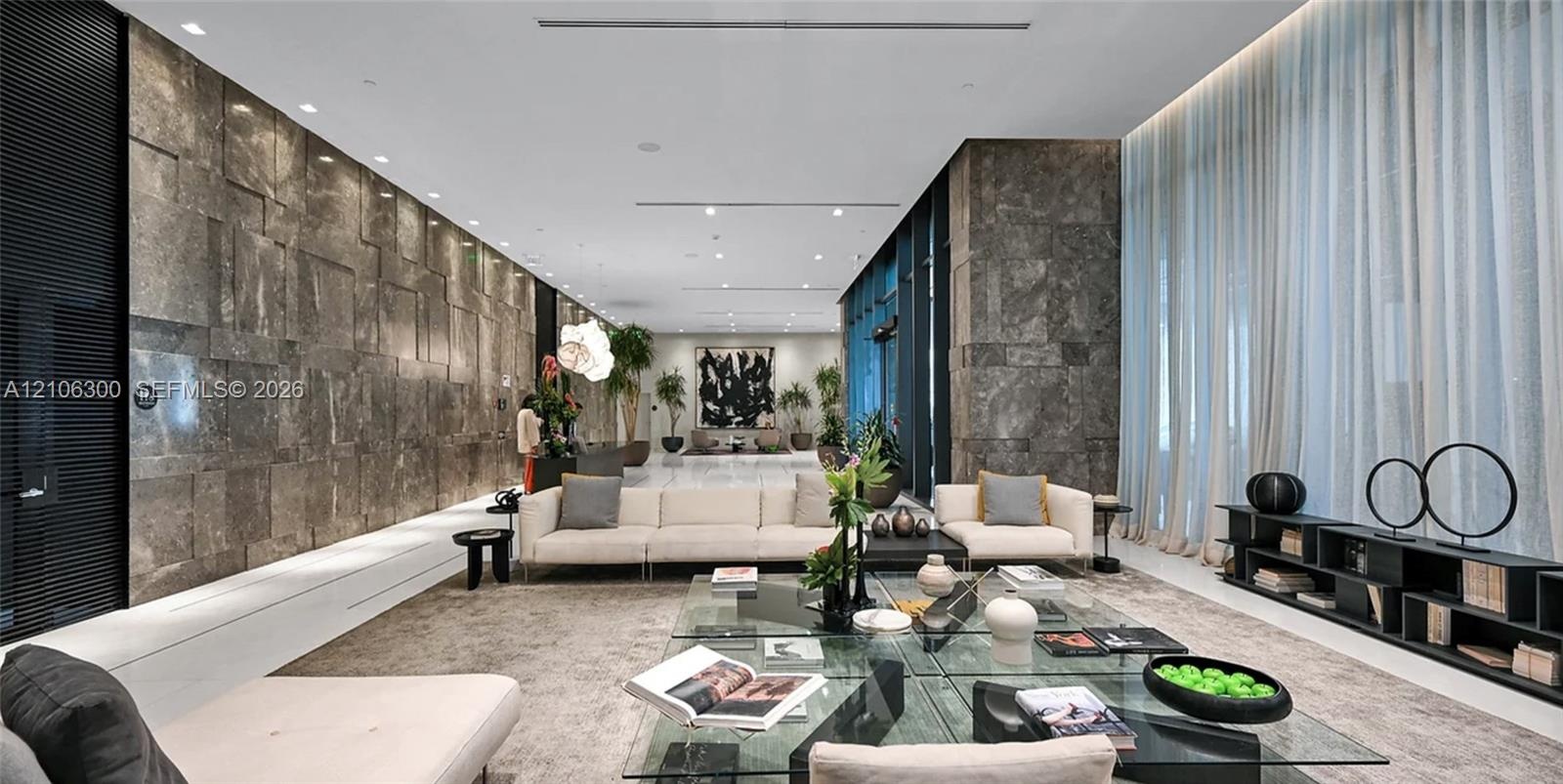 Expansive interior space featuring a large-scale natural stone wall, polished stone flooring, floor-to-ceiling sheer drapery, and recessed linear ligh