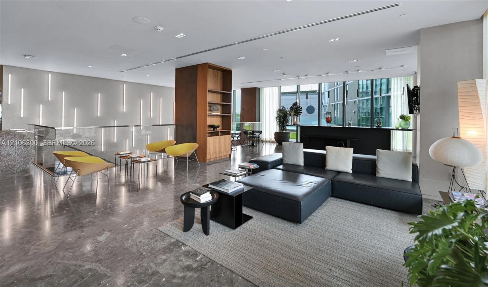 Open-concept interior featuring polished stone flooring, recessed ceiling lighting, floor-to-ceiling windows, built-in wooden shelving, and vertical w
