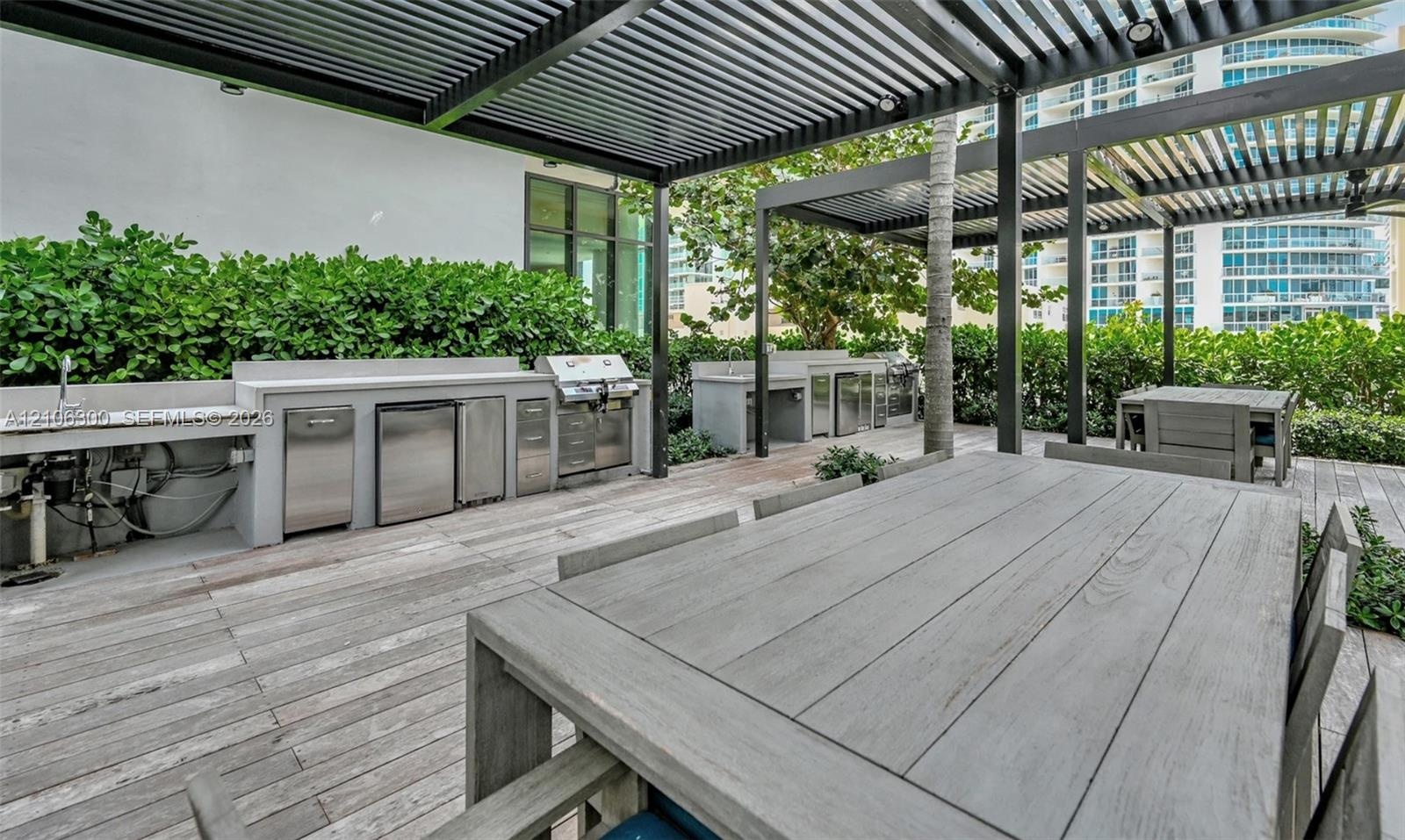 Outdoor kitchen featuring stainless steel built-in appliances, concrete-finish countertops, pergola-covered terrace, and wood-finish decking