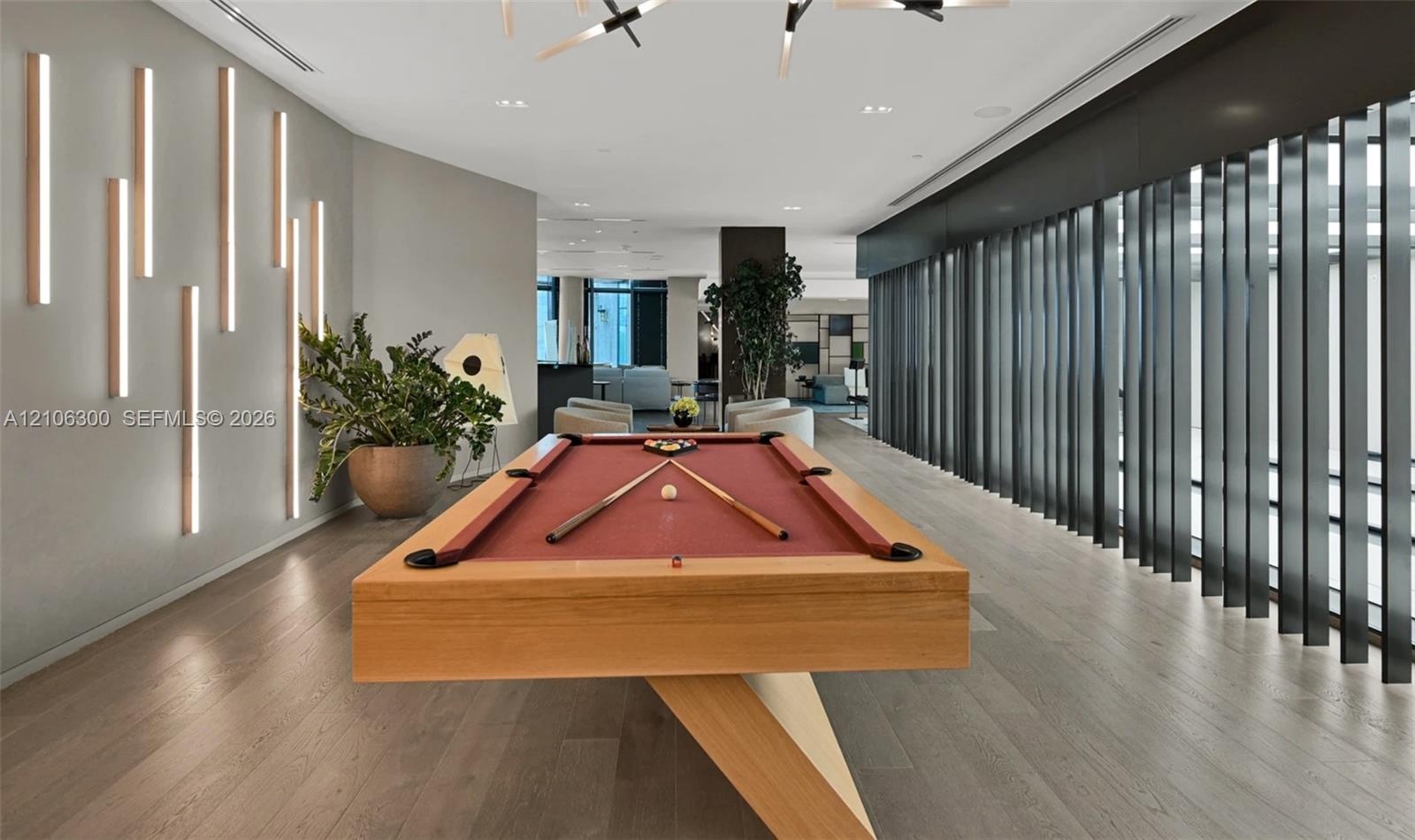 Open-concept recreational space featuring wood-finish flooring, vertical wall-mounted accent lighting, and a series of floor-to-ceiling structural fin
