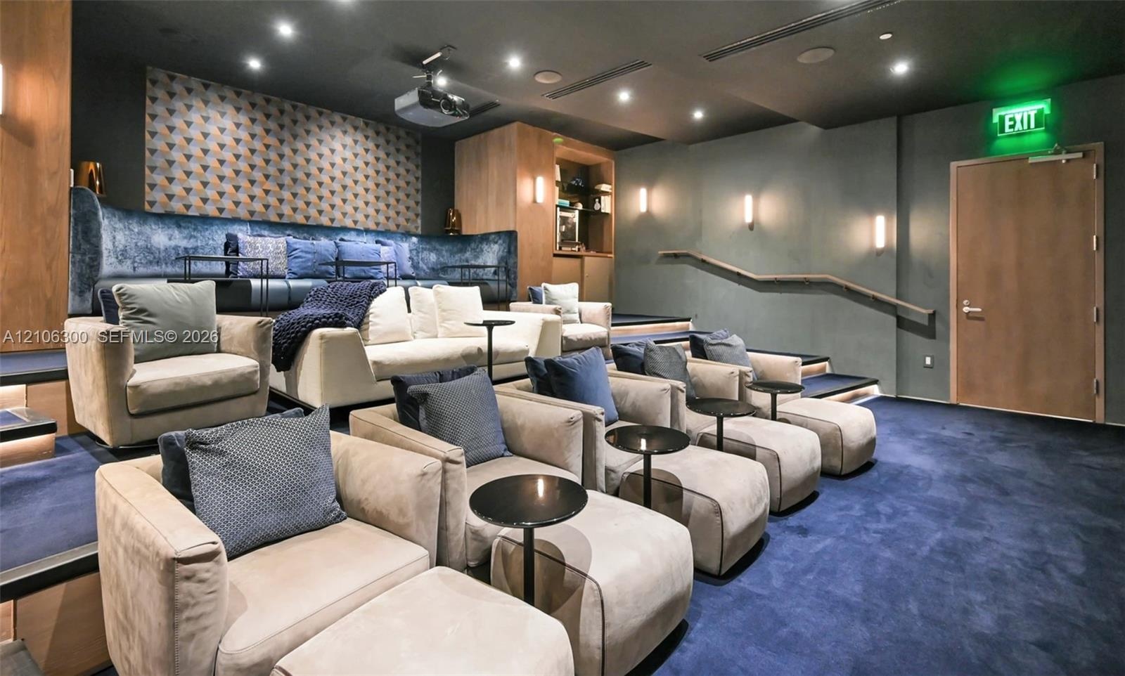 Tiered seating platform with carpeted finish, recessed ceiling lighting, wall-mounted sconces, wood-paneled wall accents, and built-in projection syst