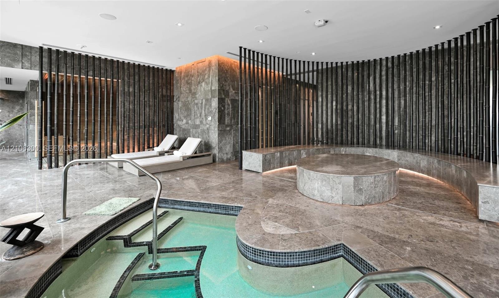 Spa area featuring stone-clad flooring and walls, curved built-in stone seating with integrated ambient lighting, circular raised stone platform, and 