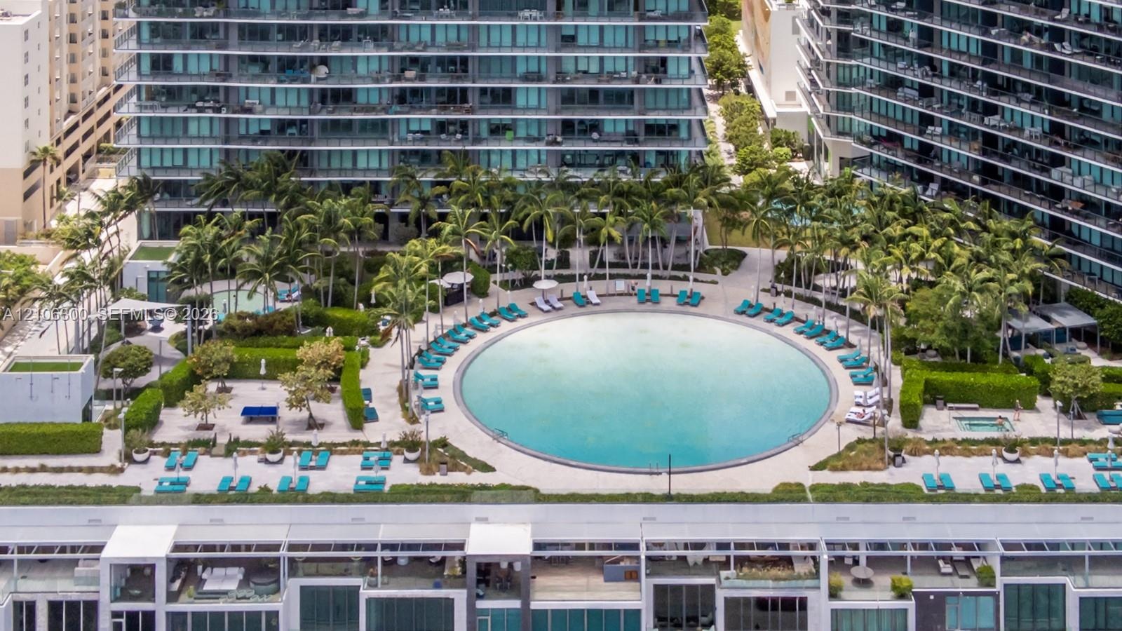 Circular swimming pool surrounded by paved decking, manicured landscaping, mature palm trees, and an integrated hot tub