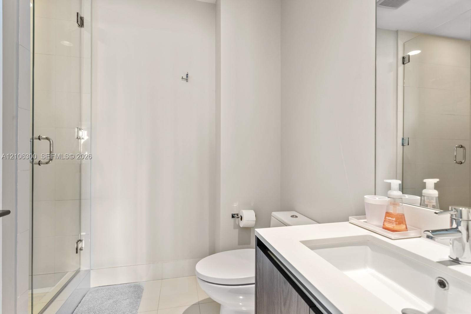 Glass-enclosed shower with tiled surround, vanity featuring an integrated sink, quartz-composite countertop, and wall-mounted mirror