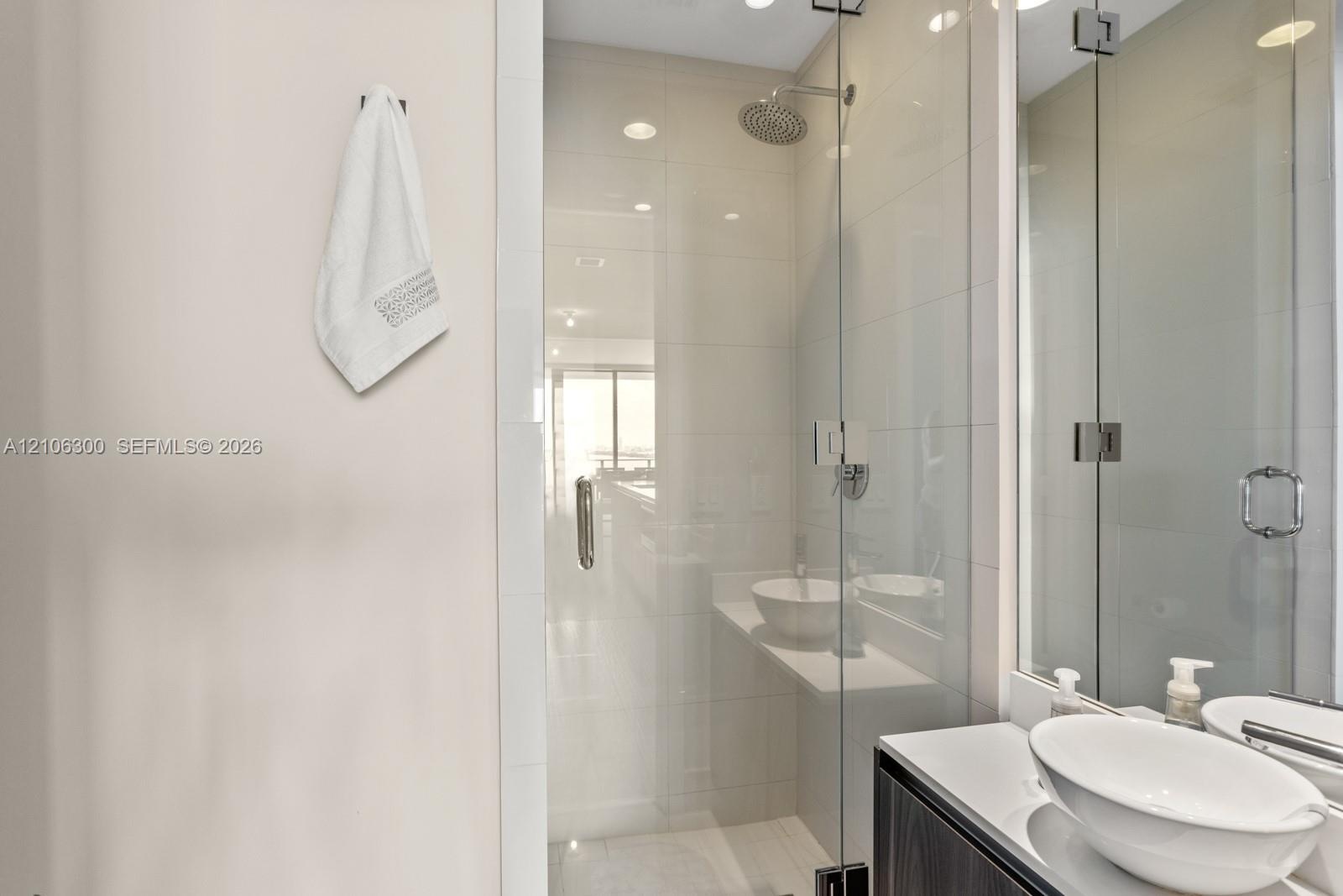 Walk-in shower with floor-to-ceiling tile, frameless glass enclosure, and a ceiling-mounted rainfall showerhead, accompanied by a floating vanity feat