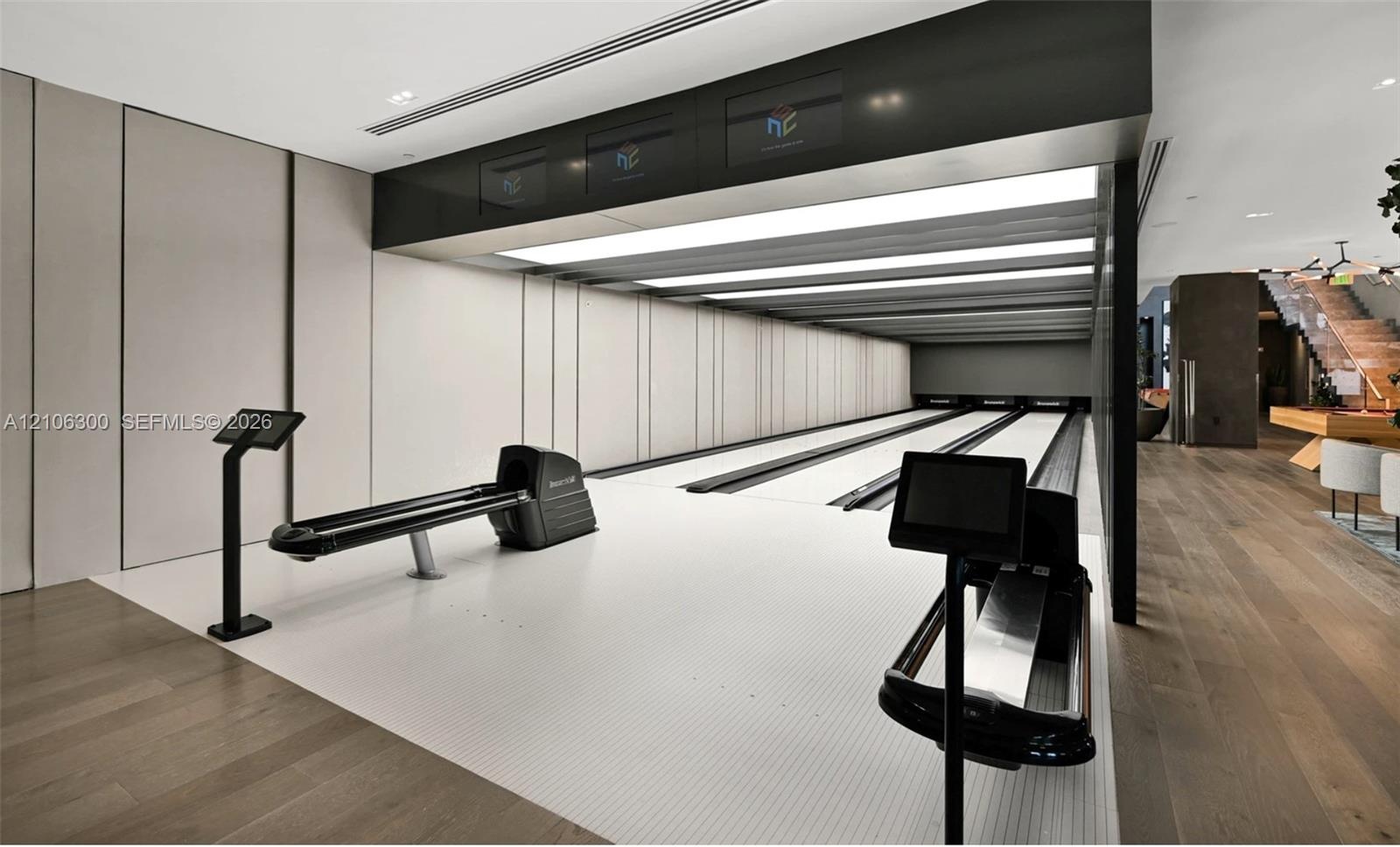 Private three-lane bowling alley featuring recessed linear lighting, integrated electronic scoring consoles, wood-finish flooring, and minimalist pane