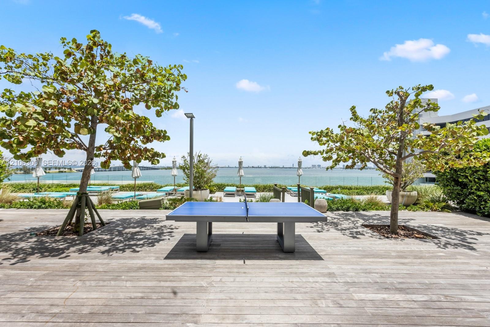 Outdoor deck featuring wood-finish decking, mature trees, and a glass perimeter railing
