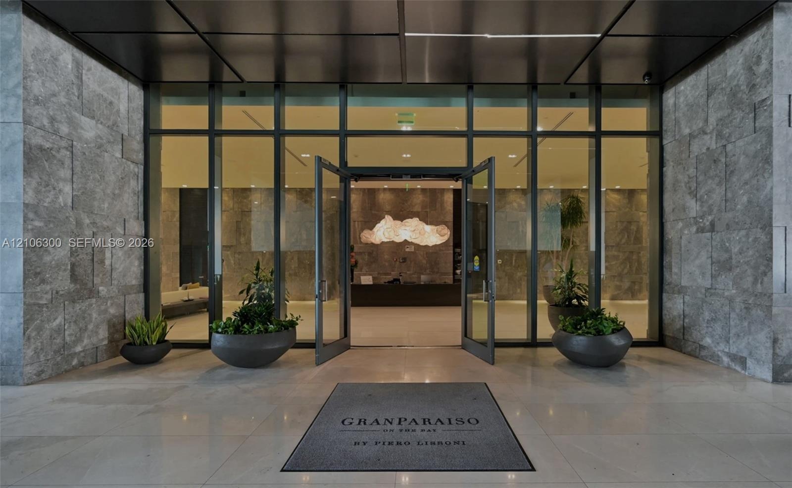 Expansive glass-paneled entrance framed by oversized textured stone cladding, polished stone flooring, and a sleek metal ceiling canopy