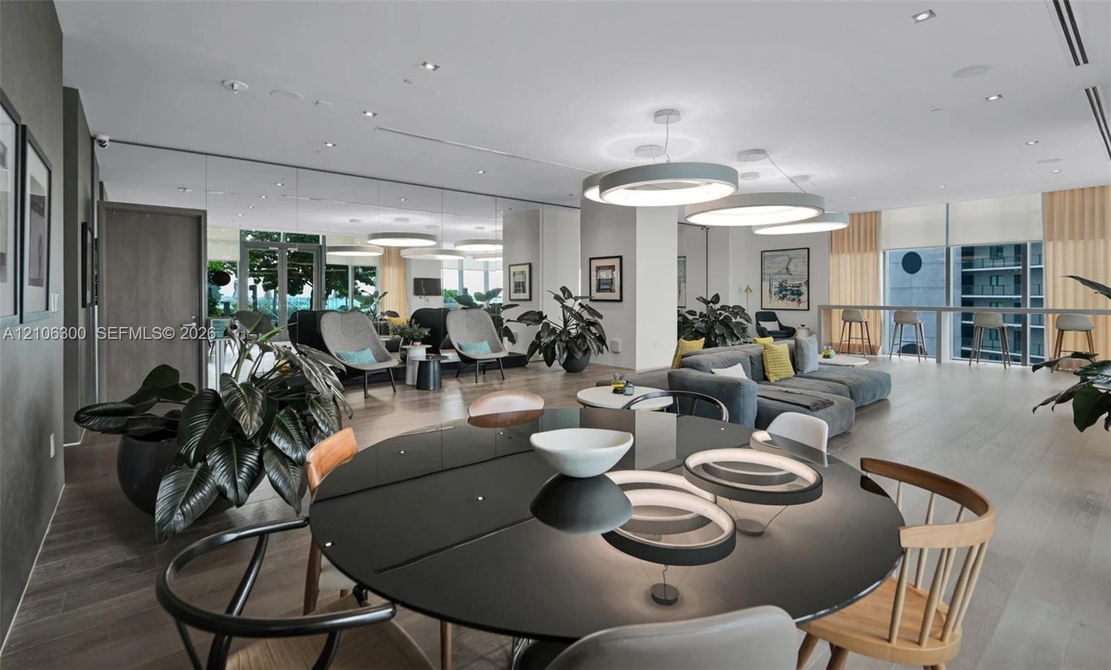 Open-concept interior featuring wood-finish flooring, recessed lighting, expansive floor-to-ceiling windows, and large circular pendant light fixtures