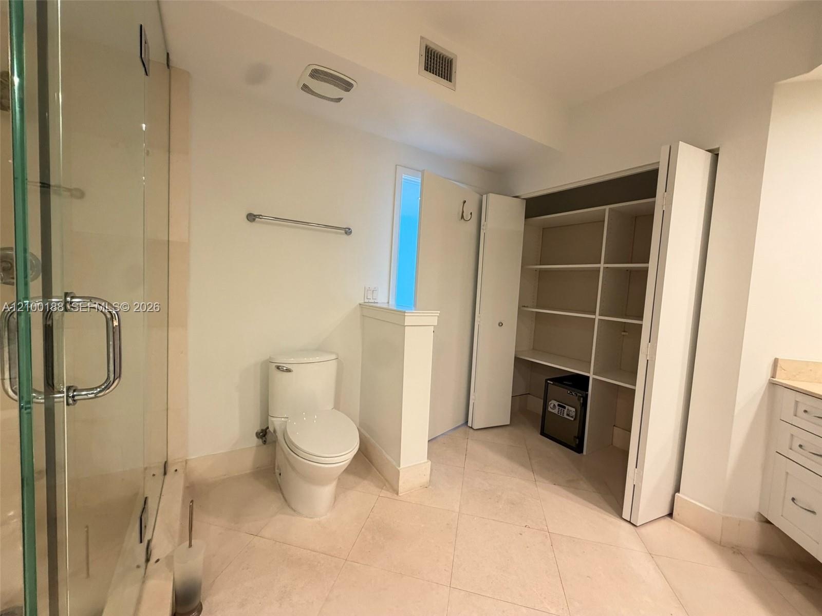 Bathroom featuring a glass-enclosed shower, tile flooring, built-in open shelving, and white cabinetry with a light-toned countertop