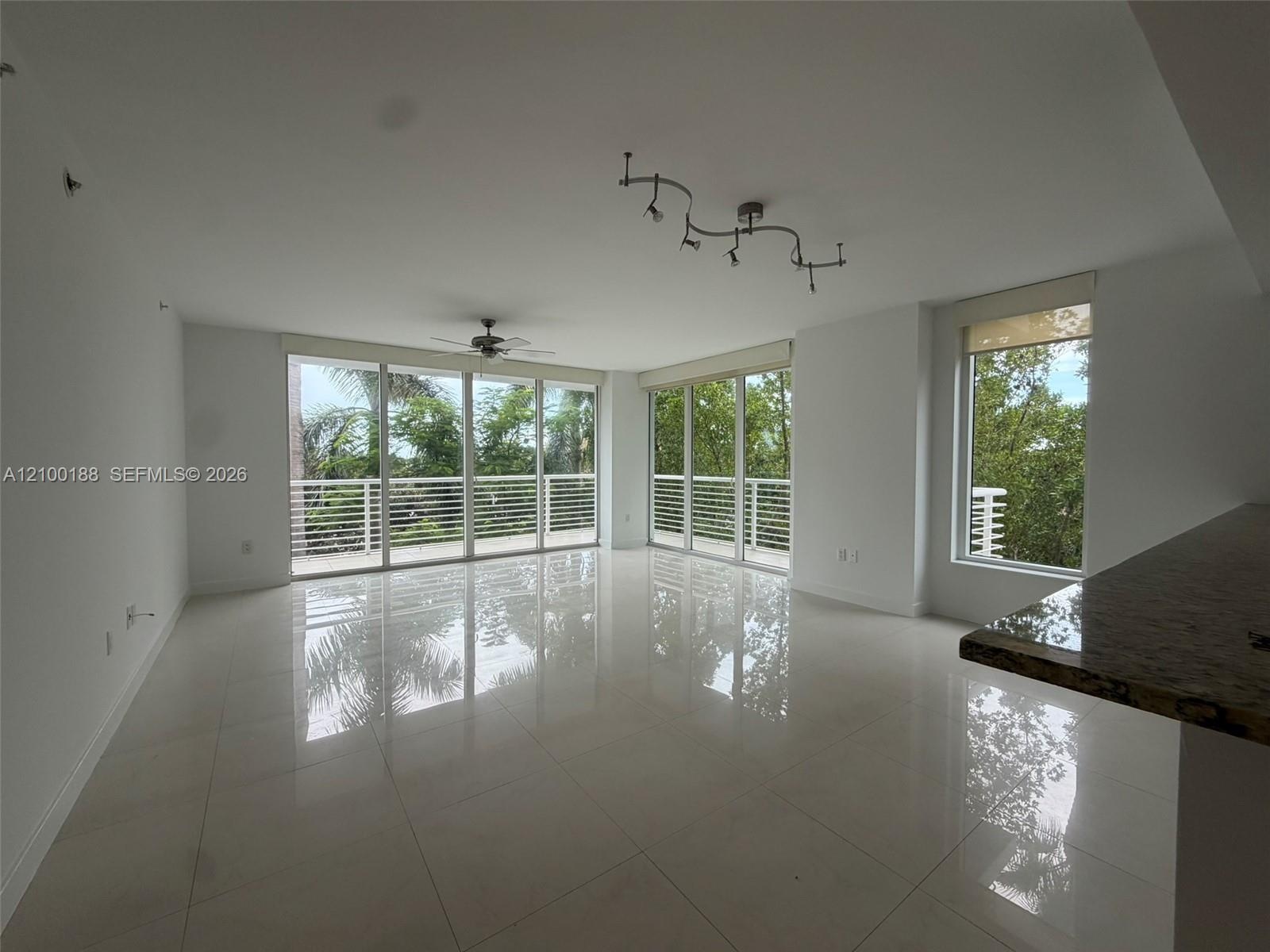 Open-concept interior featuring large-format tile flooring, expansive floor-to-ceiling glass sliding doors, integrated track lighting, a ceiling fan, 