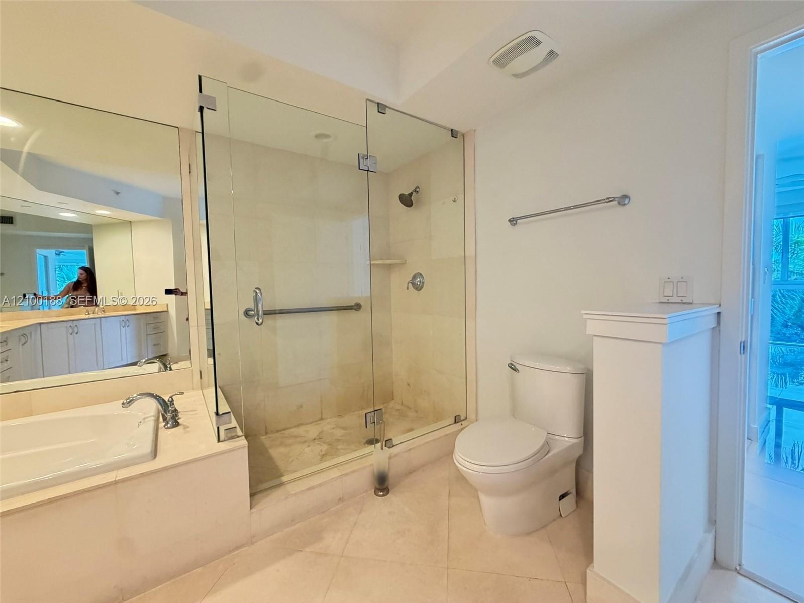Bathroom featuring a tiled shower stall with a glass enclosure, built-in soaking tub with stone surround, wall-to-wall vanity mirror, and neutral tile