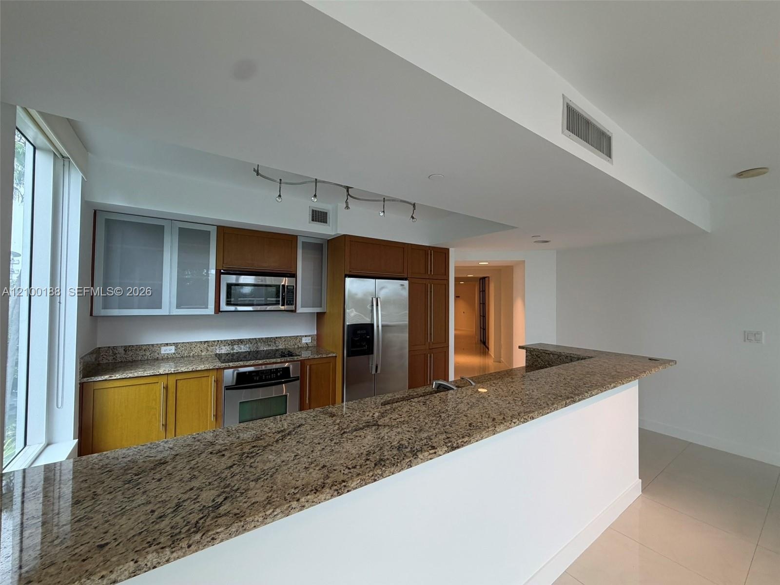 Kitchen featuring wood cabinetry, stone countertops, stainless steel appliances, a breakfast bar, and tile flooring