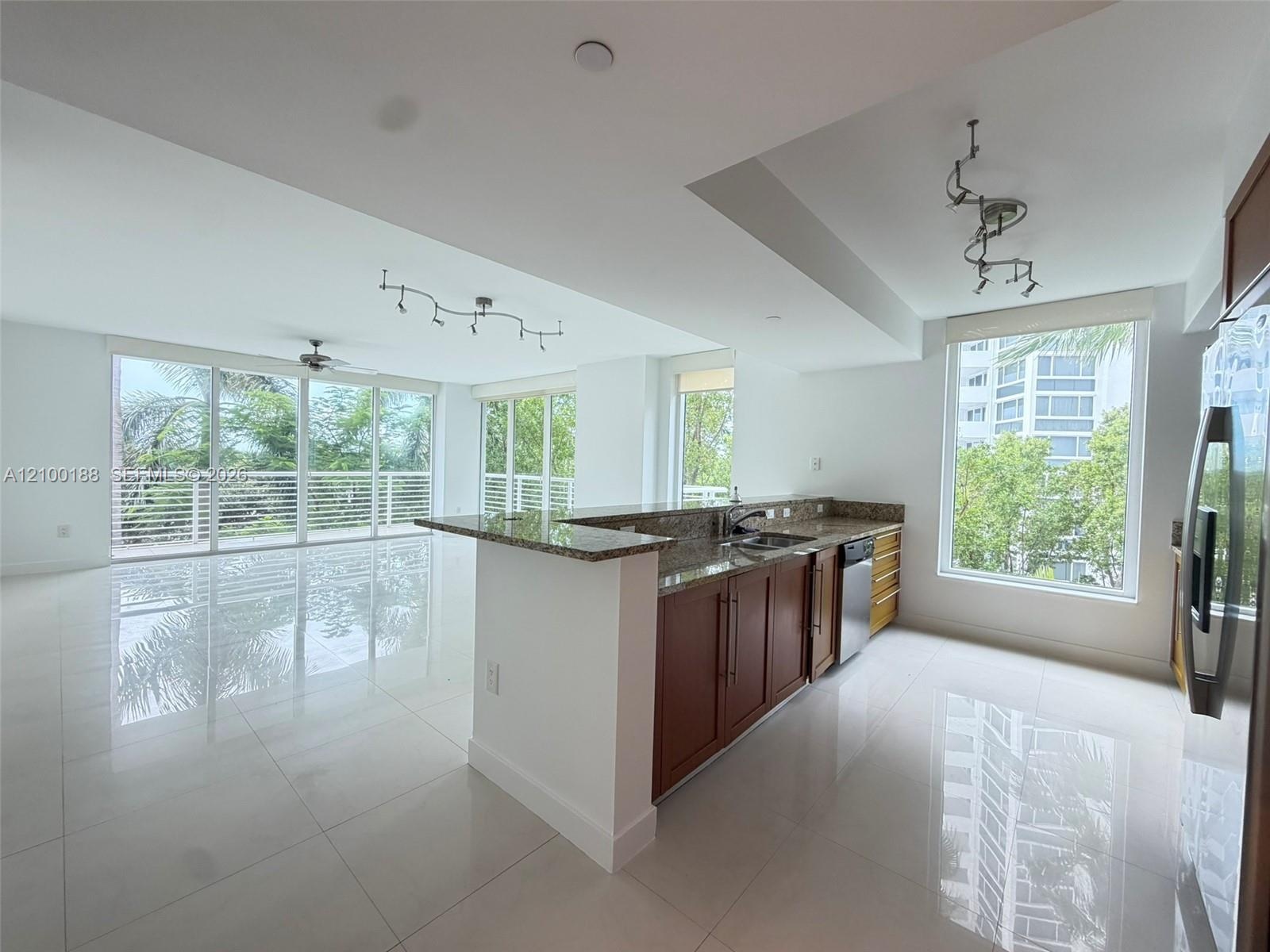 Open concept kitchen featuring stone countertops, wood-finish cabinetry, stainless steel appliances, large-format tile flooring, and floor-to-ceiling 