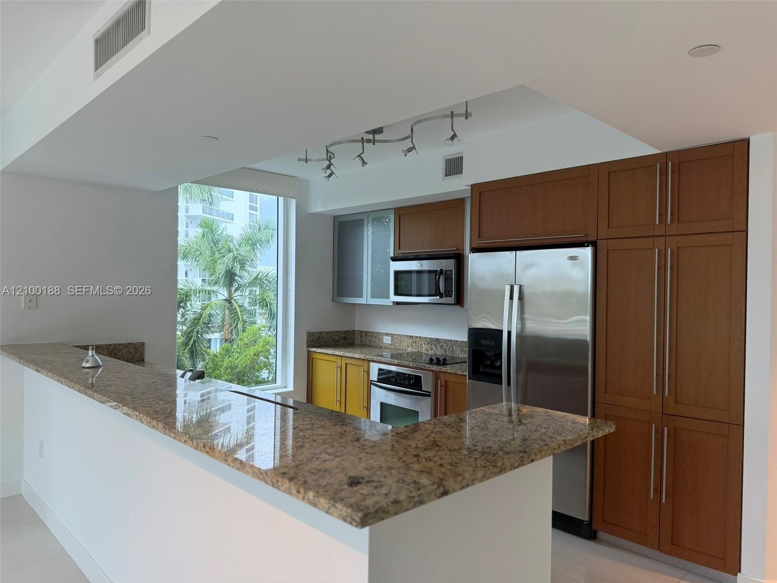 Kitchen featuring stone countertops, breakfast bar, built-in cabinetry with glass-panel upper doors, stainless steel appliances, and track lighting