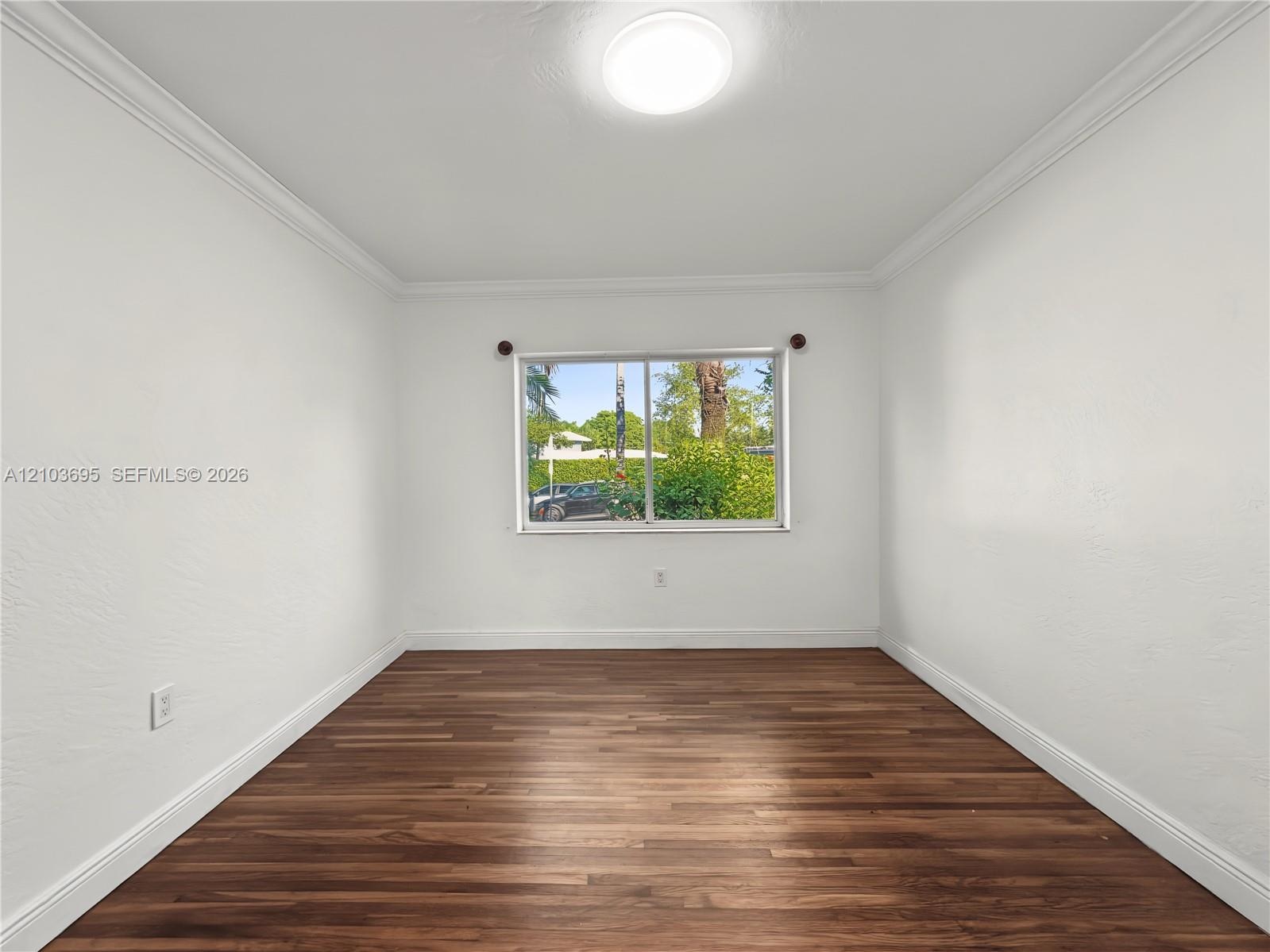 Interior space featuring wood-finish flooring, white walls, crown molding, and a dual-pane sliding window