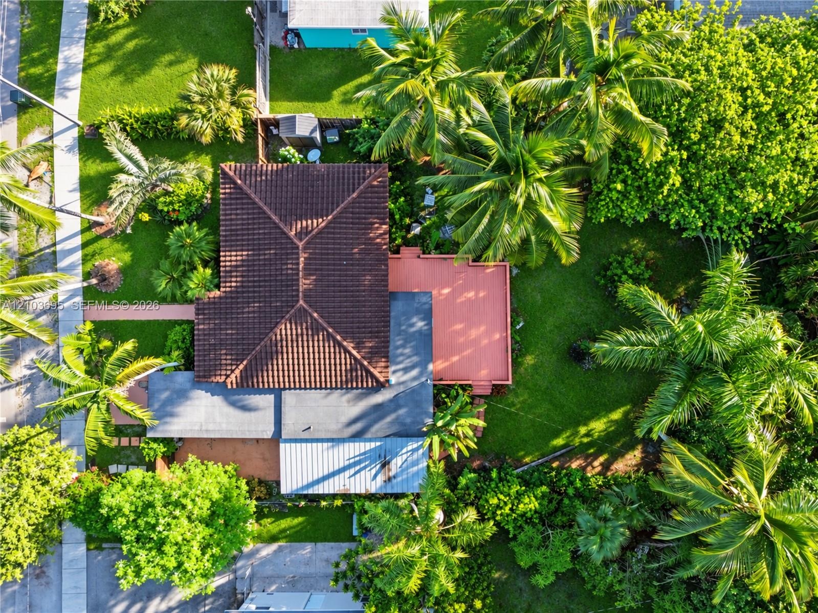 Aerial view of a property featuring a tile roof, an elevated wooden deck, mature palm trees, and extensive landscaping