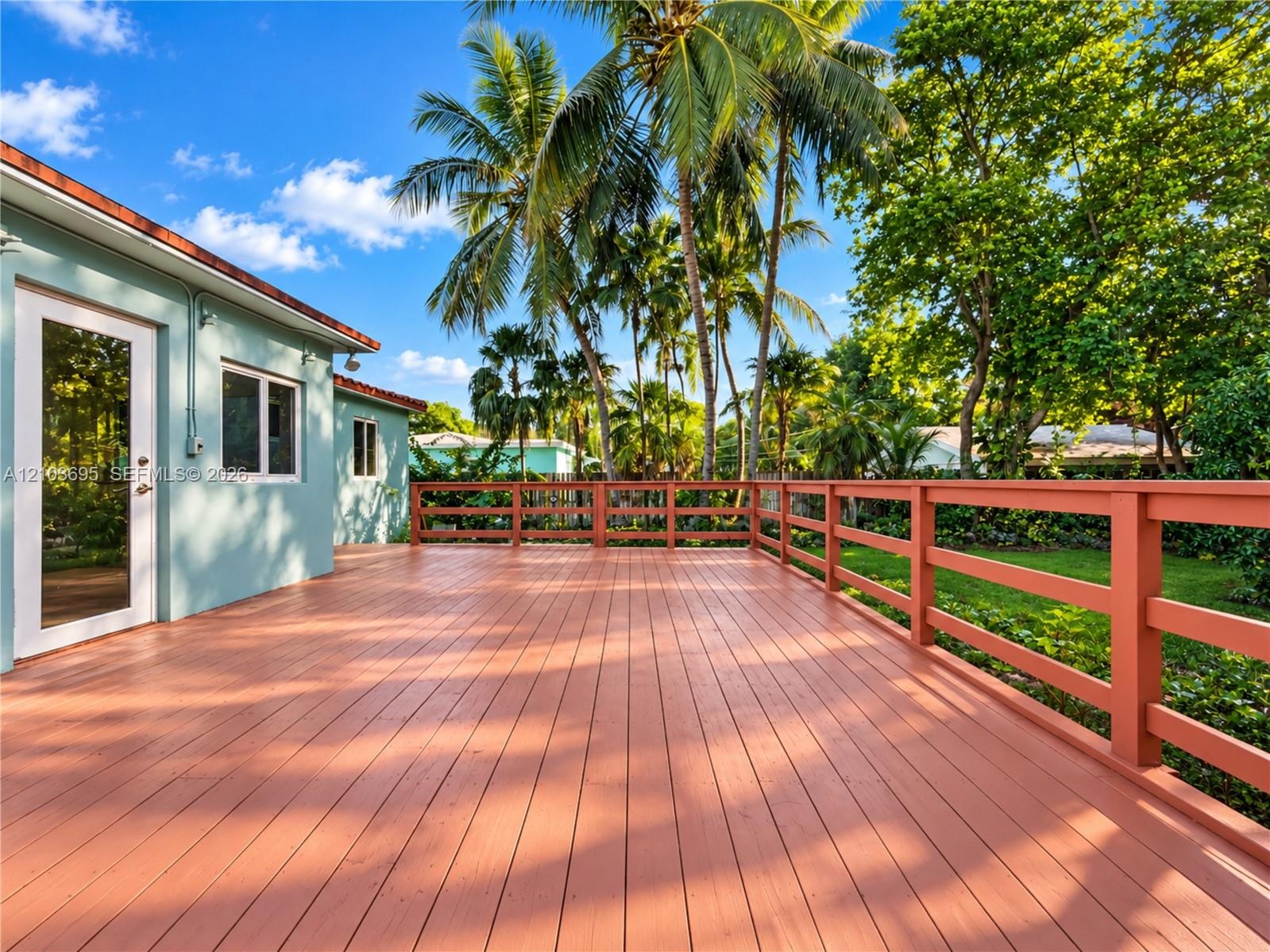Expansive wooden deck featuring horizontal rail fencing, mature palm trees, and structural exterior access