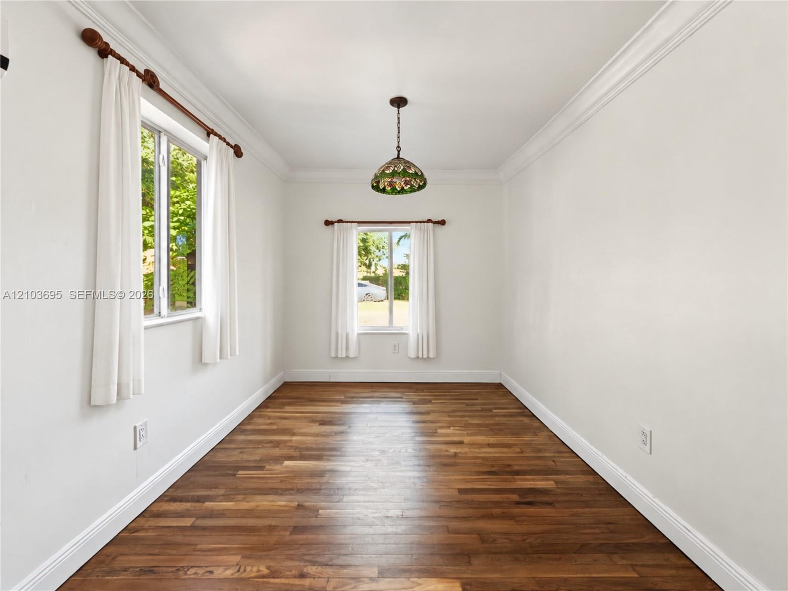 Room featuring wood-finish flooring, crown molding, dual windows, and a decorative pendant light fixture