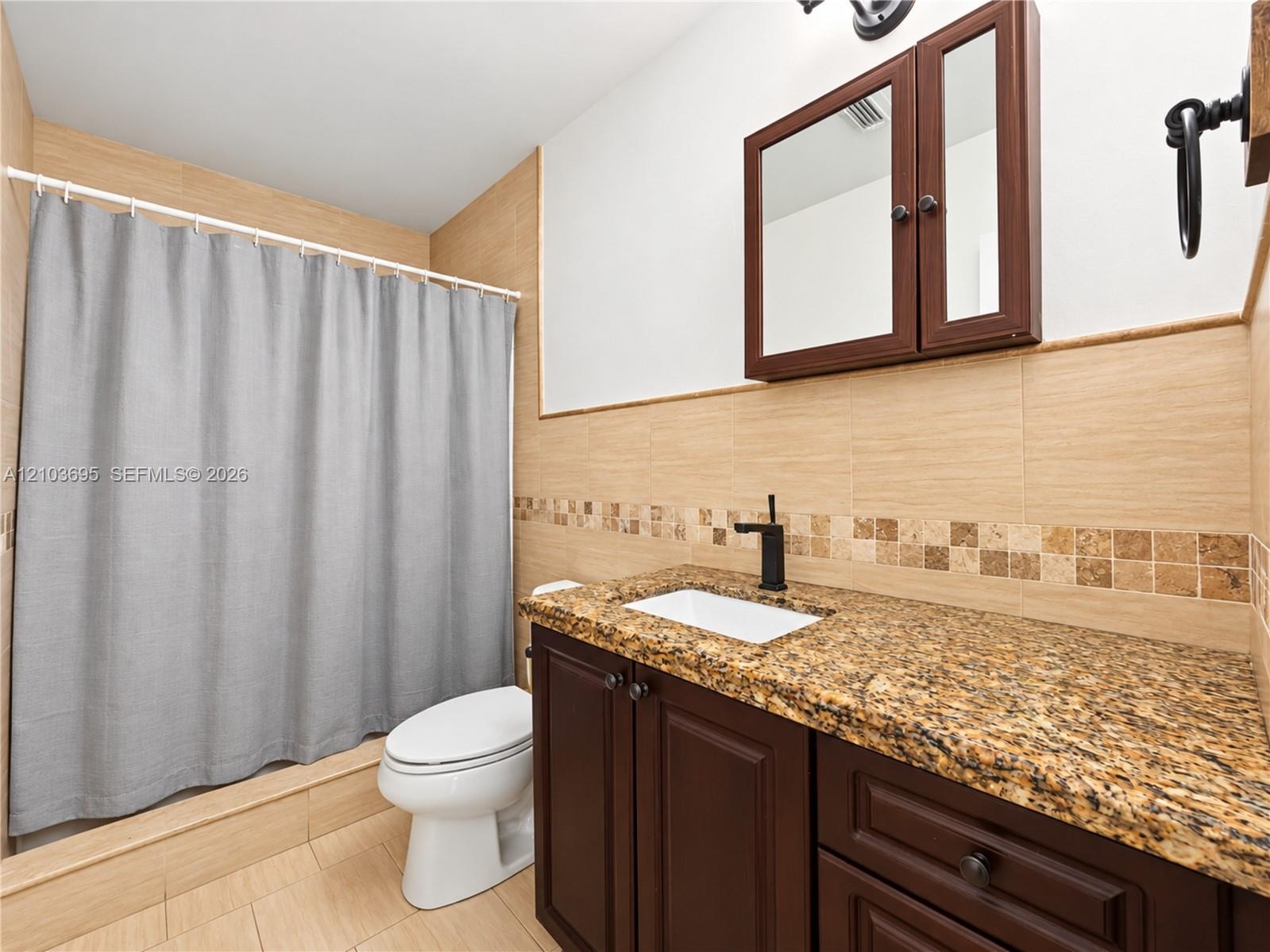 Bathroom featuring stone-surface vanity with rectangular undermount sink, dark wood-finish cabinetry, built-in medicine cabinet, matte black hardware,