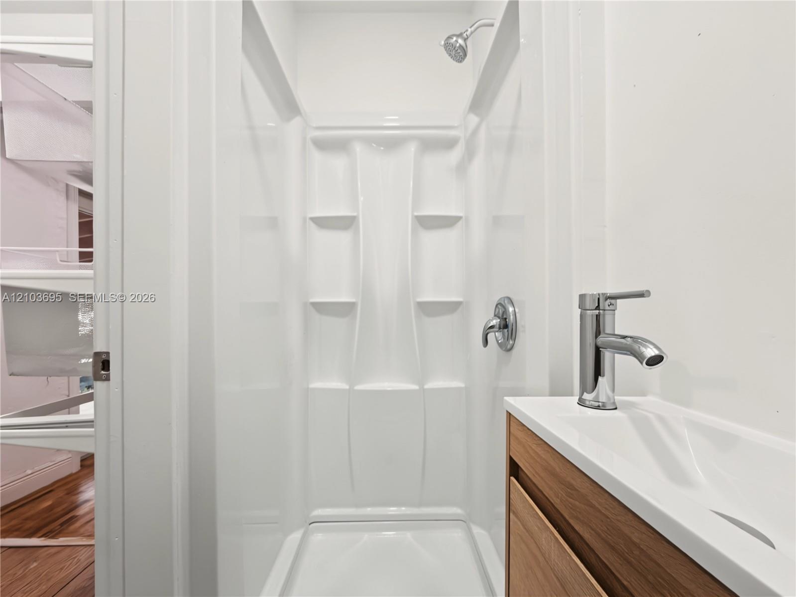 Shower stall with integrated shelving, chrome shower head, wood-finish vanity with a rectangular basin, and single-handle chrome faucet