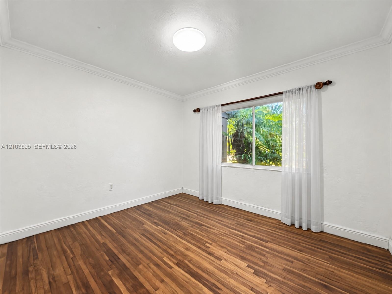 Room featuring wood-finish flooring, crown molding, and a sliding window with outdoor greenery exposure