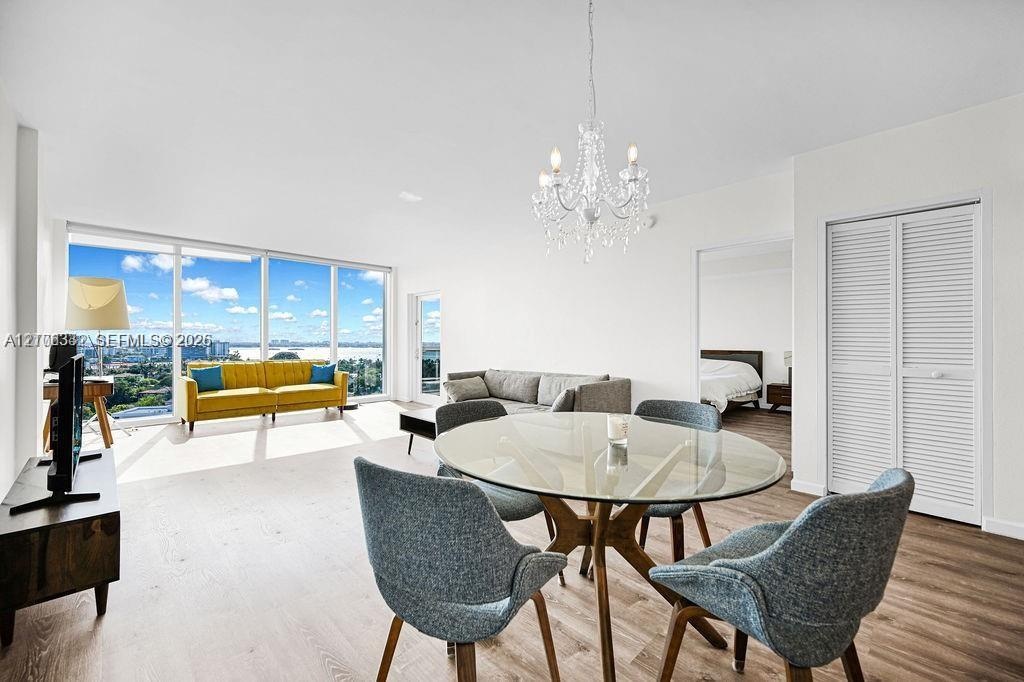 Open-concept living space featuring floor-to-ceiling windows, wood-finish flooring, a crystal chandelier, and louvered closet doors