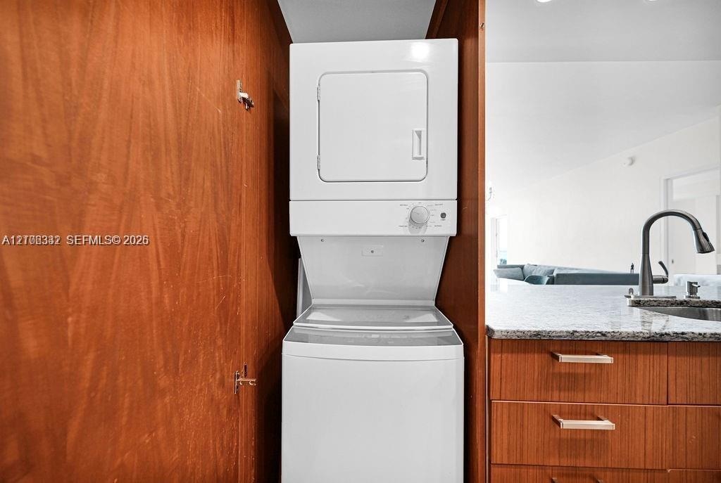 Stacked laundry unit housed within wood-finish cabinetry, featuring stone-surface countertop, flat-panel drawers with horizontal hardware, and a high-
