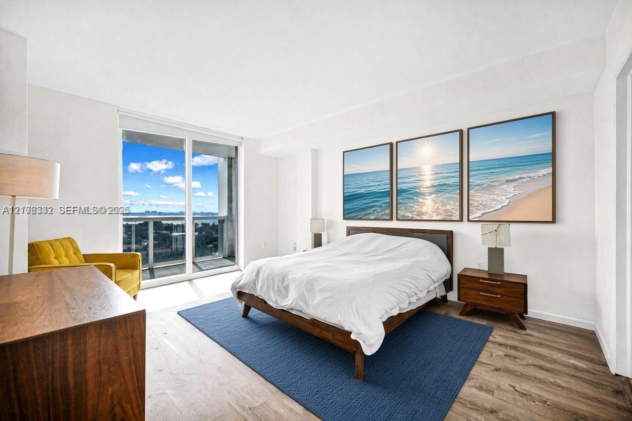 Floor-to-ceiling glass sliding doors with access to an exterior balcony, wood-finish flooring, and expansive water scenery