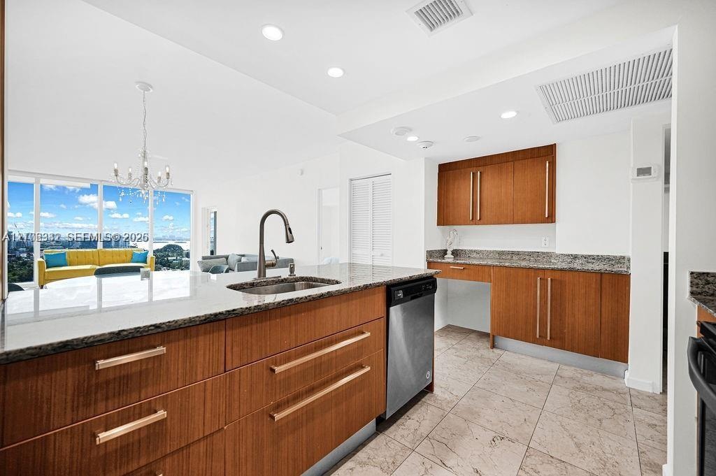Kitchen featuring wood-finish cabinetry with linear pulls, stone-surfaced countertops, a stainless steel undermount sink with a gooseneck faucet, stai