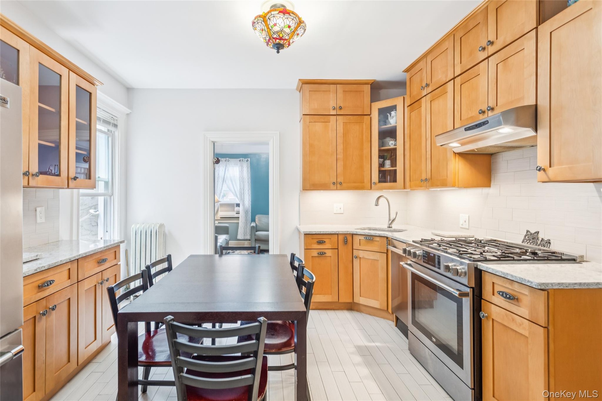 Kitchen with stainless steel range with gas cooktop, under cabinet range hood, radiator heating unit, tasteful backsplash, and light stone countertops