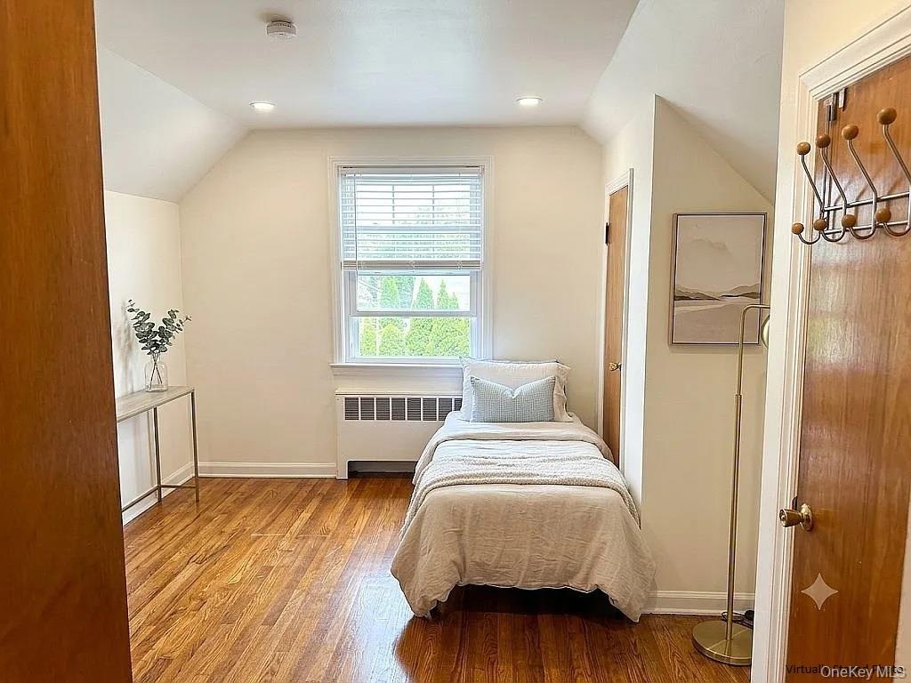 Room with hardwood flooring, recessed ceiling lighting, a window with horizontal blinds, and a custom-fitted radiator cover