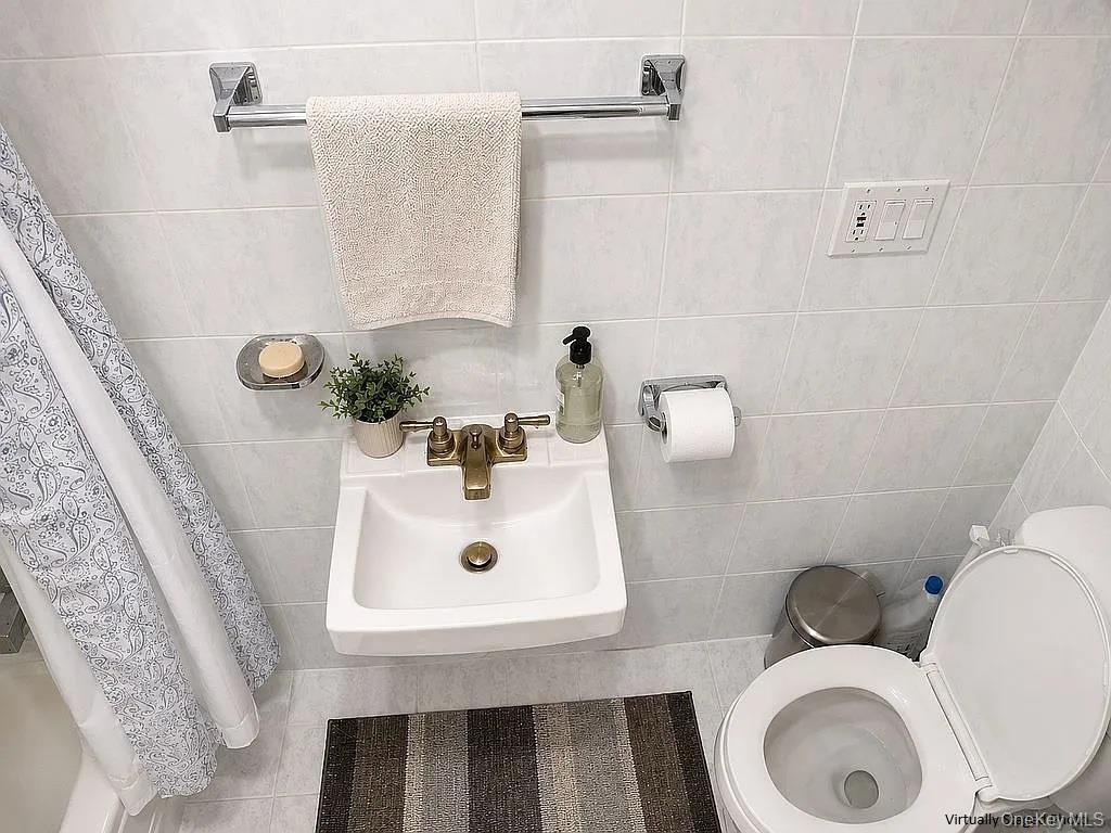 Wall-mounted porcelain sink featuring a metallic dual-handle faucet, surrounded by floor-to-ceiling white ceramic wall tile and chrome-finish bathroom