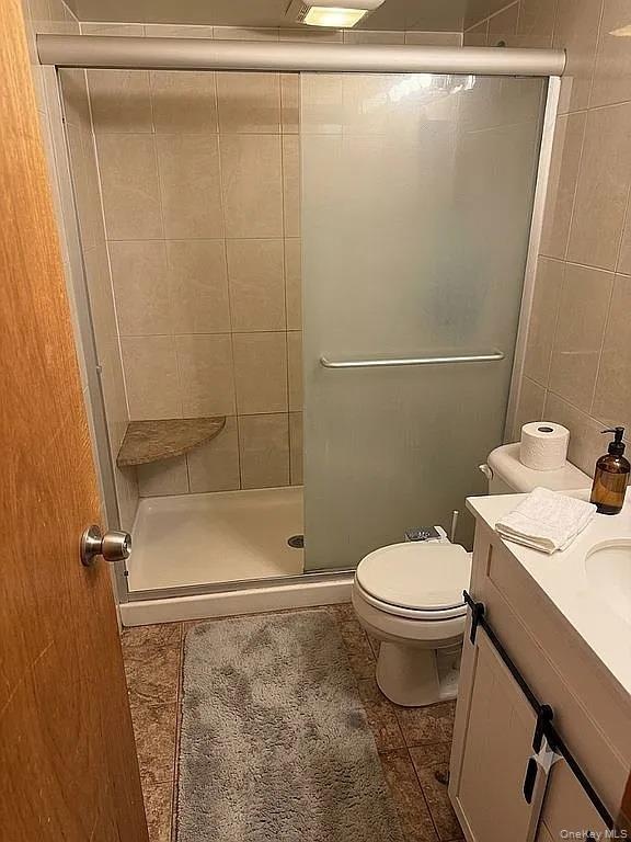 Shower stall featuring a built-in corner bench, sliding frosted glass doors, and wall tile surround, paired with a white vanity featuring a solid surf