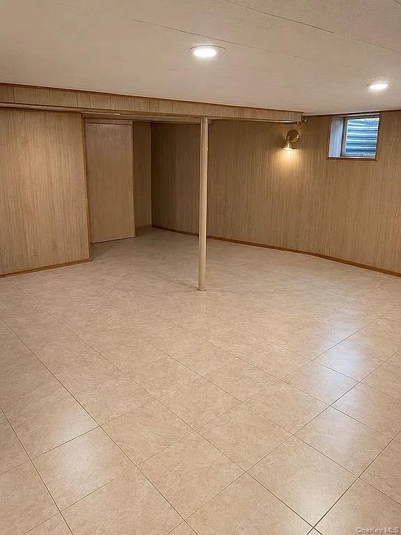 Finished lower-level space featuring tile flooring, vertical wood-panel wall finishing, recessed ceiling lighting, and a structural support column