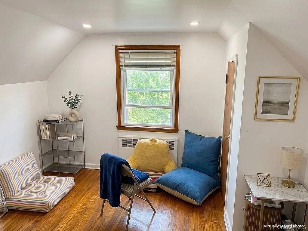 Sloped ceiling architecture featuring wood-finish flooring, a centrally positioned window with wood trim, and recessed lighting