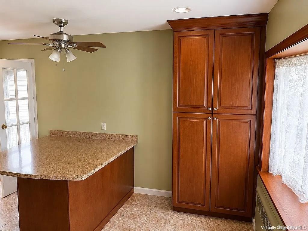 Custom wood-finish floor-to-ceiling cabinetry, stone-texture countertop, wood-finish breakfast bar, and brushed-metal ceiling fan with integrated ligh