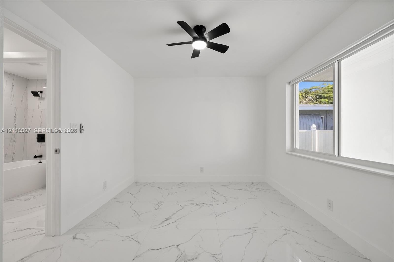 Large-format stone-style tile flooring with veining detail, integrated matte black ceiling fan with light, and wide sliding window