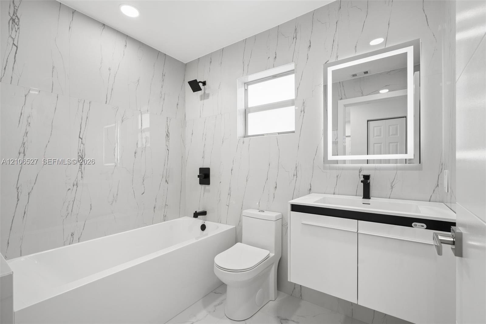 Modern bathroom featuring floor-to-ceiling large-format tile, a floating vanity with a vessel sink, a matte black faucet and shower head, and a built-