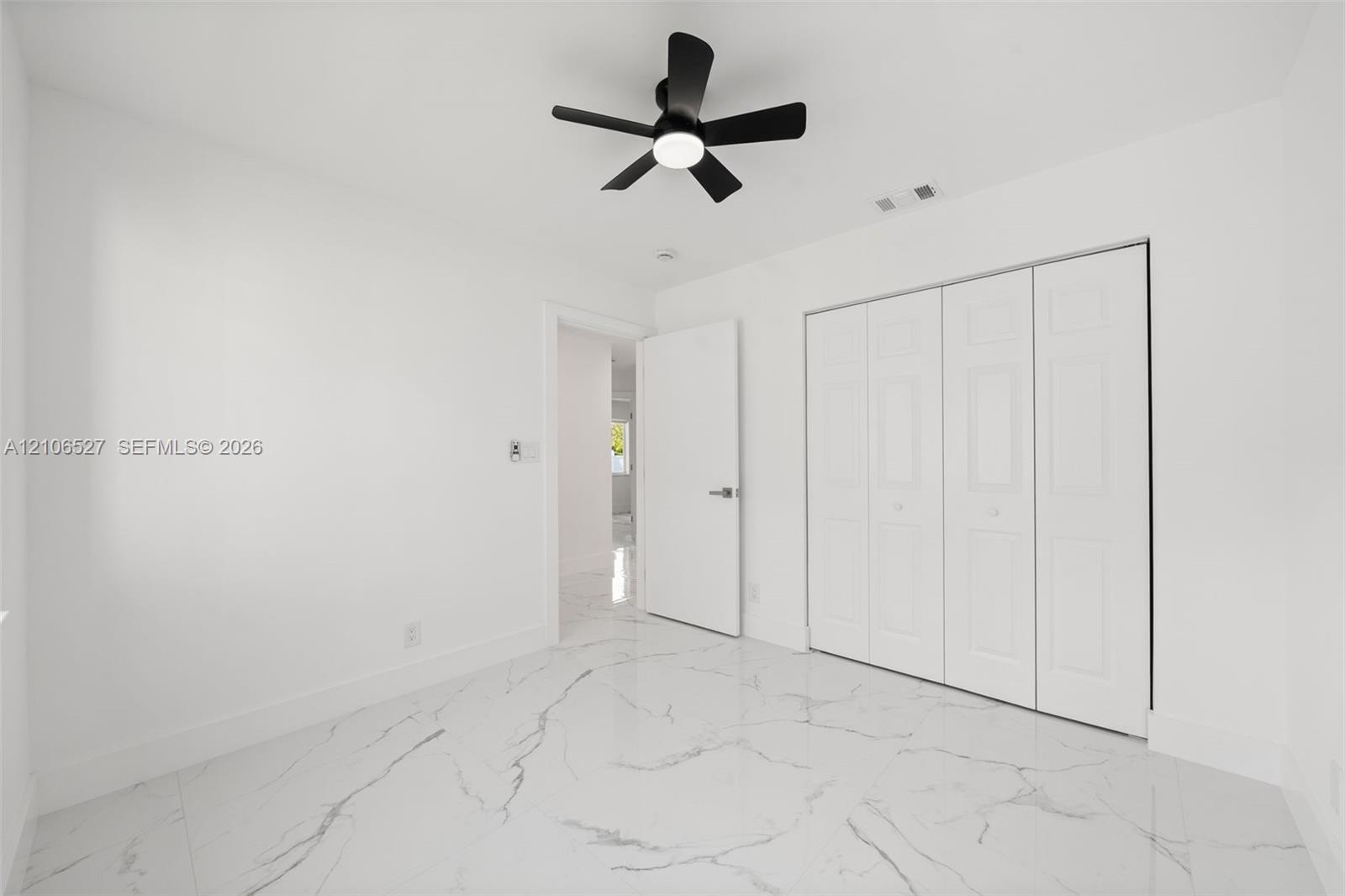 Interior room featuring white-veined large-format tile flooring, a matte black ceiling fan with integrated lighting, and white bi-fold closet doors