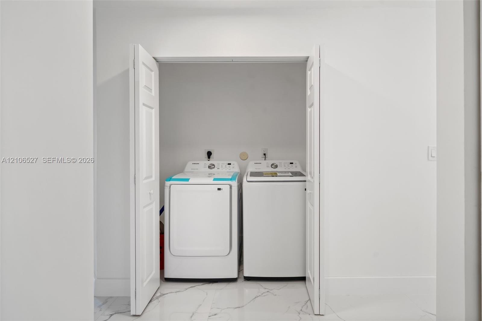 Laundry alcove featuring white bi-fold doors, white interior walls, and tile flooring