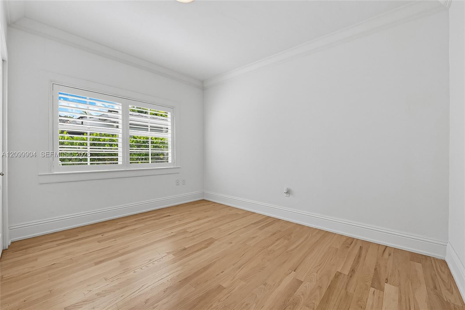 Interior space featuring wood-finish flooring, crisp white walls, crown molding, and plantation shutters