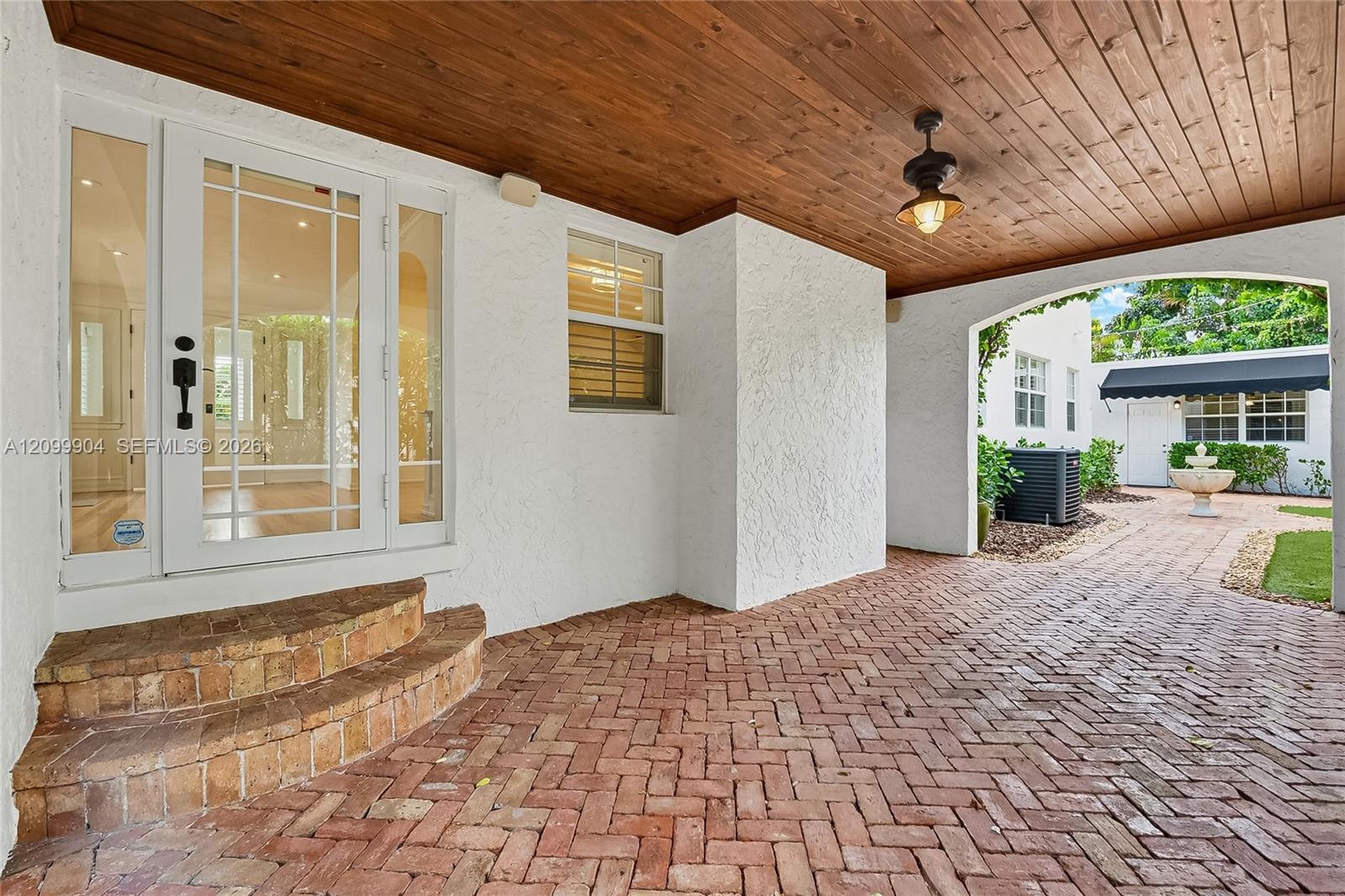 Covered entryway featuring a wood-plank ceiling, herringbone brick paving, and a glass-paneled entry door with sidelights