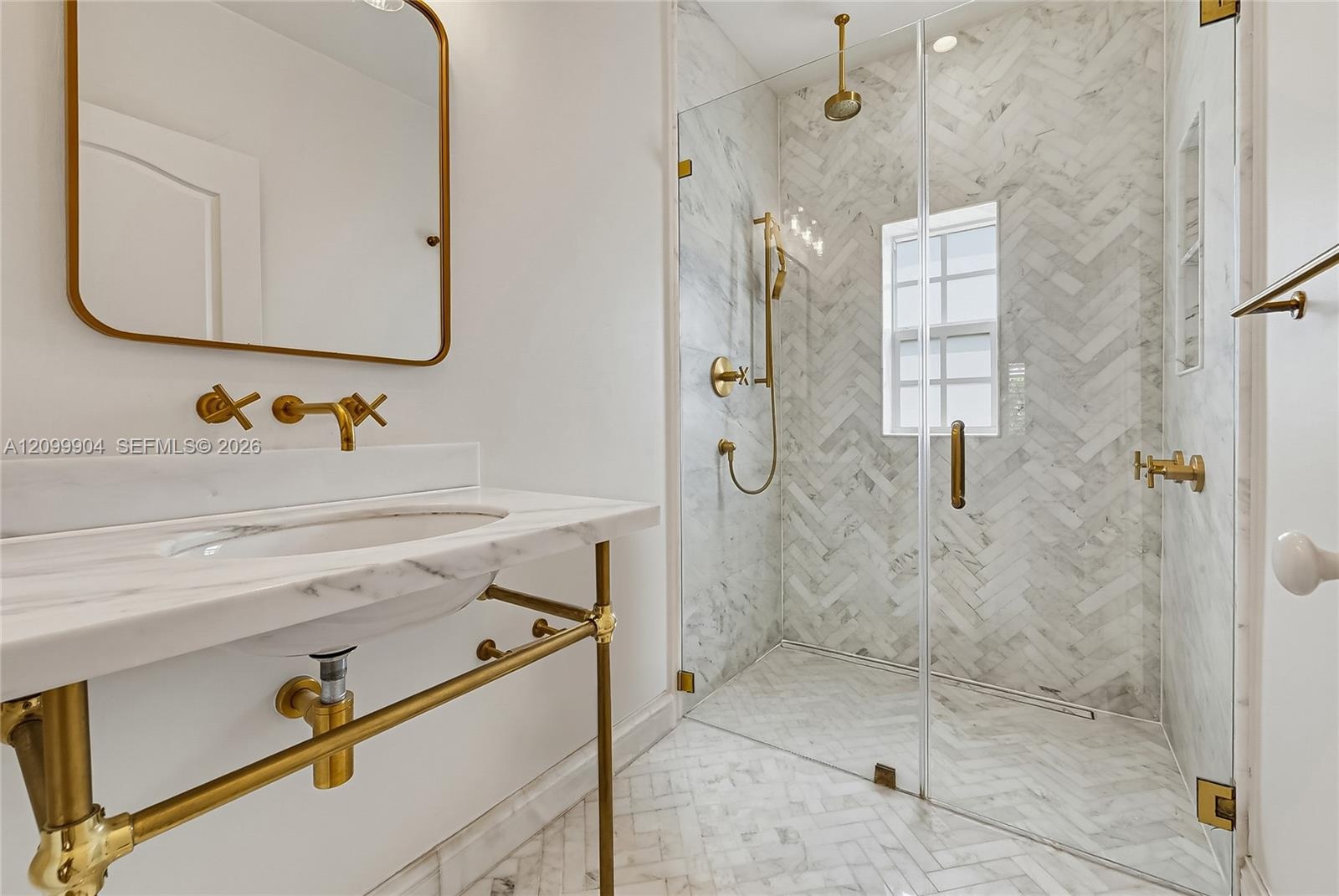 Console-style vanity with a stone countertop and brass-finish plumbing fixtures, glass-enclosed walk-in shower featuring herringbone tile pattern, and