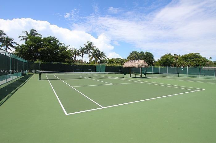 Hard-court tennis facility featuring perimeter fencing and a thatch-roofed cabana