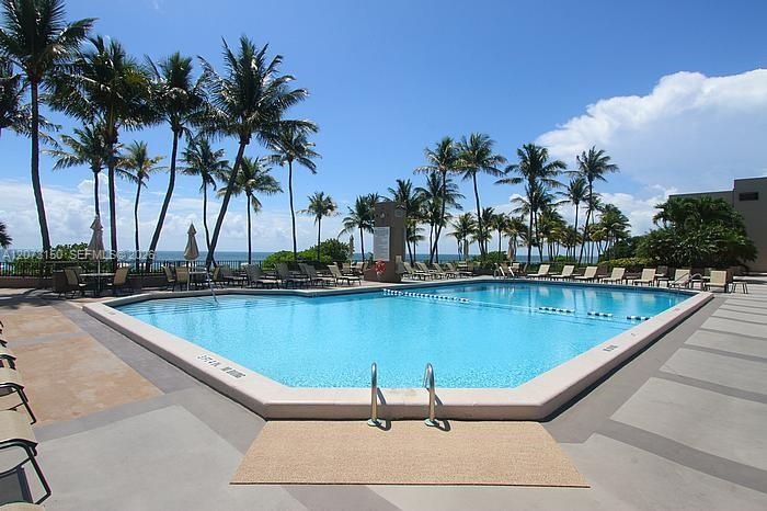 In-ground swimming pool featuring a concrete deck, metal pool ladders, and tropical palm tree landscaping