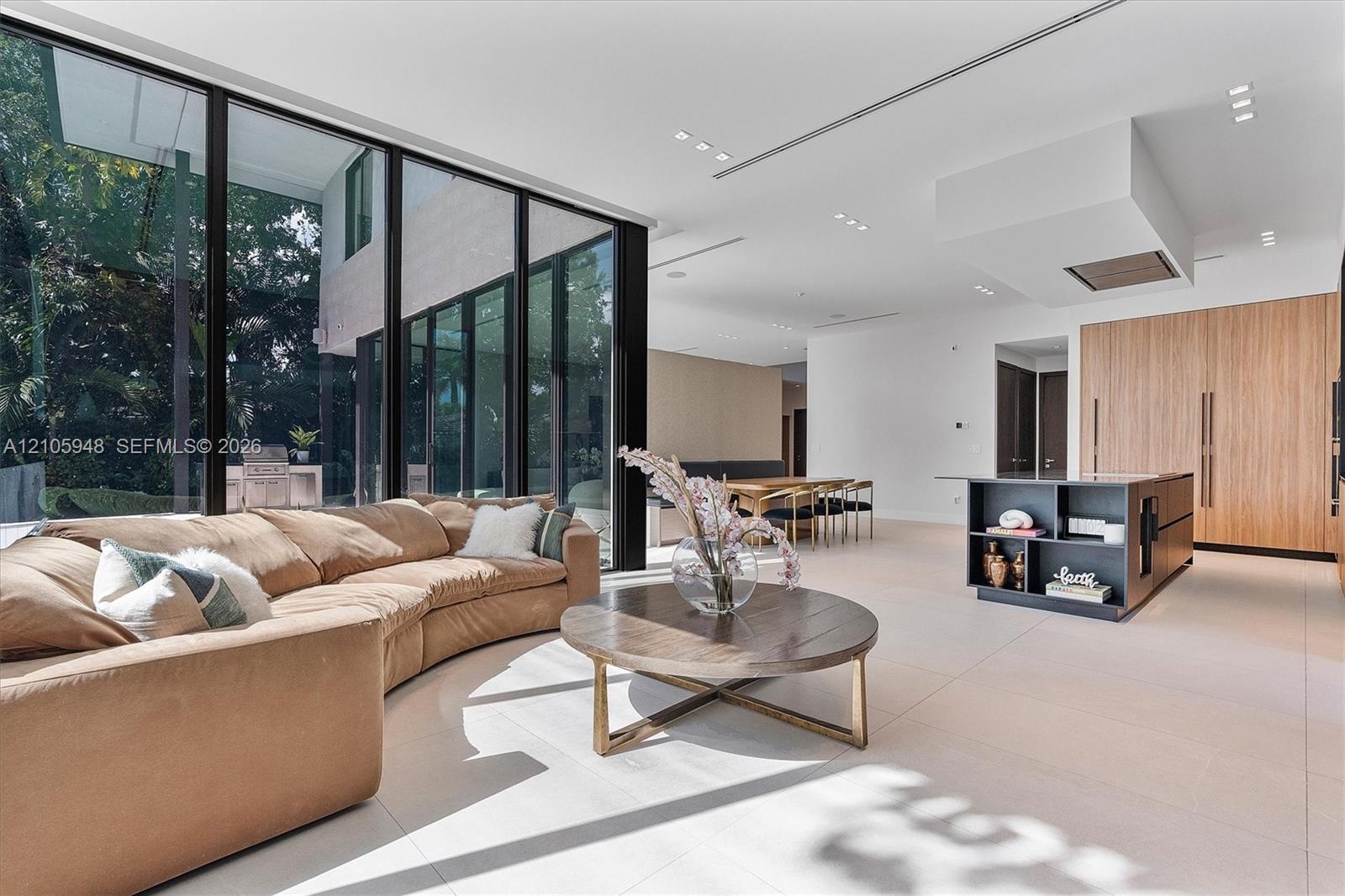 Floor-to-ceiling glass walls, integrated light-toned cabinetry, a modern kitchen island with built-in shelving, recessed ceiling lighting, and large-f