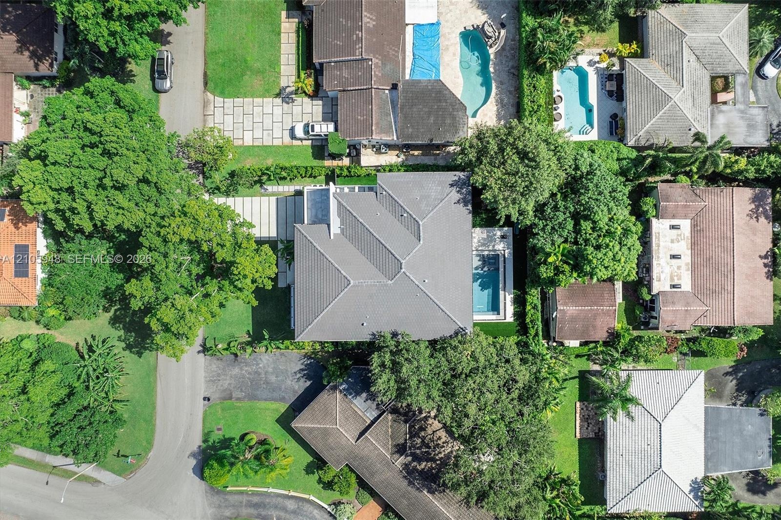 Aerial perspective featuring a hip-roof structure, rectangular swimming pool, paved driveway, and mature landscaping