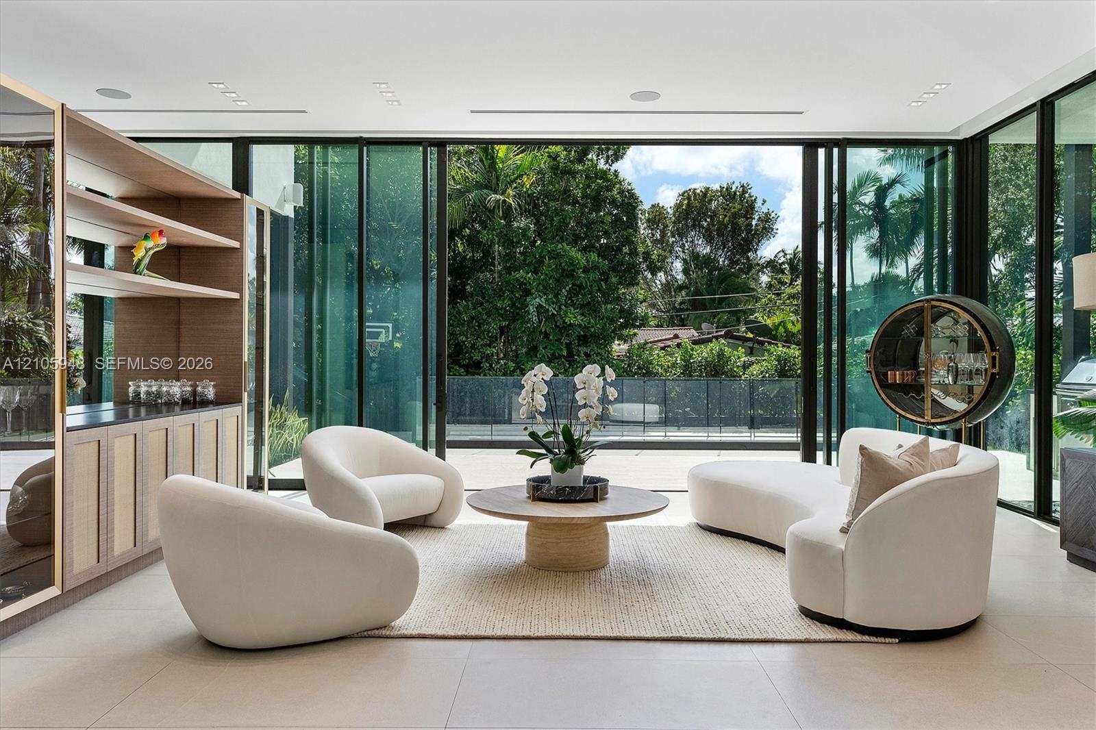Floor-to-ceiling retractable glass walls, built-in recessed ceiling lighting, light-toned large-format tile flooring, and custom wood-paneled cabinetr